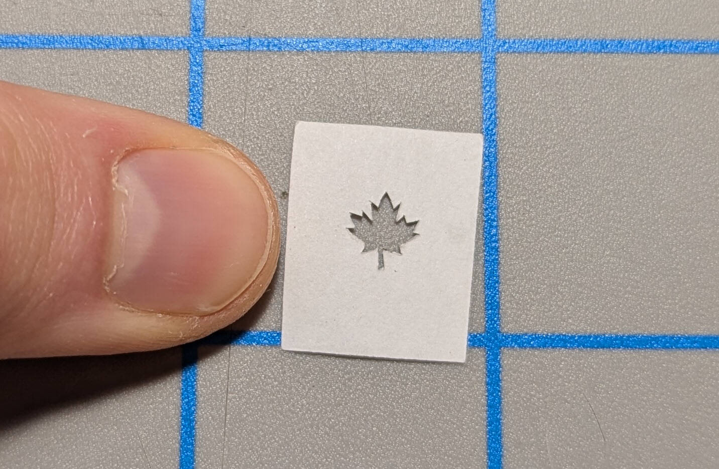 a hand cut paper maple leaf stencil, about half the width of a thumbnail